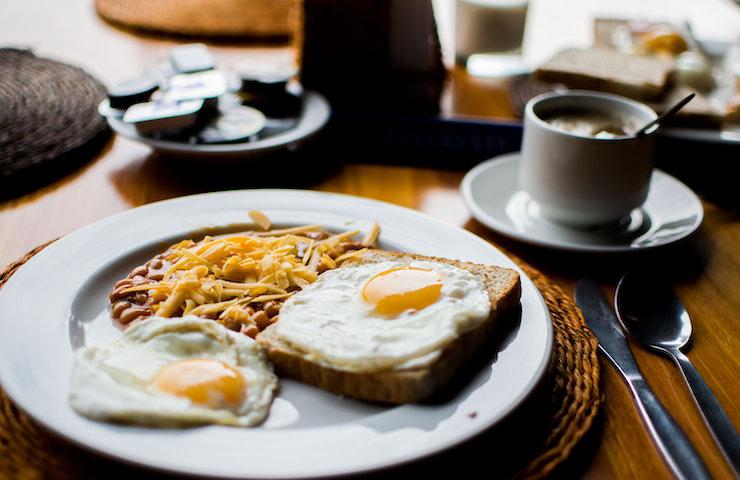 Colazione all'inglese: caffè lungo, due toast con uova all'occhio di bue, fagioli cotti e formaggio fuso