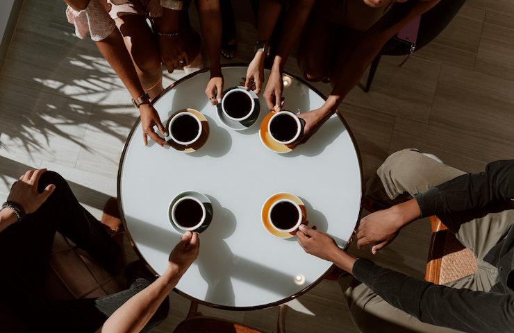 Gruppo di amici beve delle tazze di caffe seduti a un tavolo rotondo